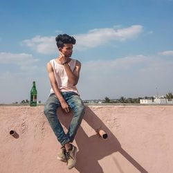 Young man sitting on land against sky