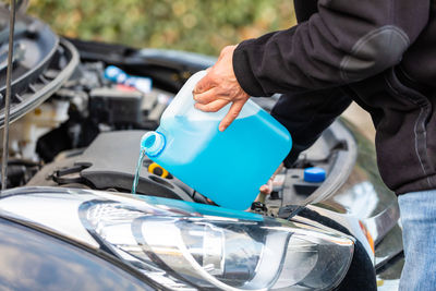 Midsection of man pouring liquid in breakdown car