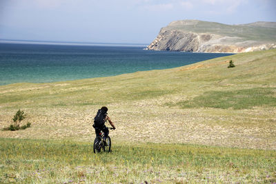 Man cycling on field against river