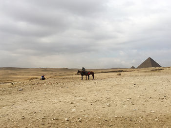 People riding horses on desert against sky