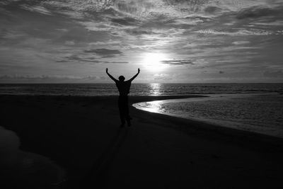 Woman with arms outstretched standing at sea shore against sky