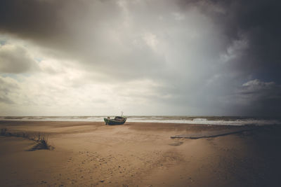 Boat at beach against cloudy sky