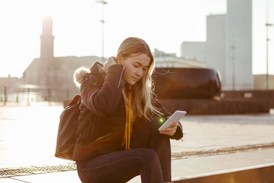 Teenage girl using smart phone while sitting on steps during sunny day