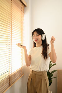 Side view of young woman standing against window