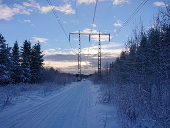 Electricity pylon by snow covered trees against sky