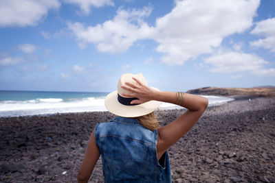 Rear view of woman standing on beach against sky