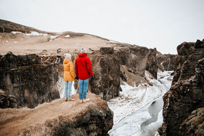 Rear view of people on rock against sky during winter