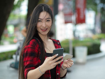 Smiling young woman using mobile phone in city