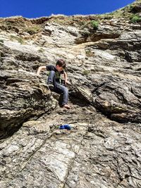 Young man standing on rock against sky