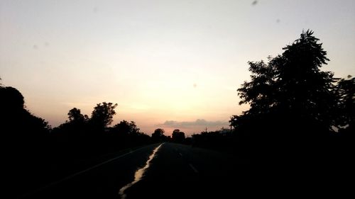 Road amidst silhouette trees against sky during sunset