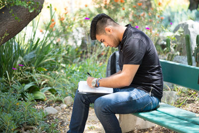 Portrait of young man sitting on bench writing