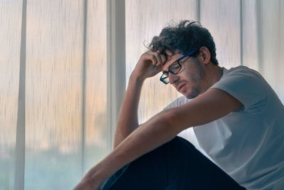 Depressed man sitting by curtain at home