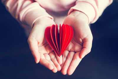  kid hands holding red paper folded heart dark background. valentines day holiday. 