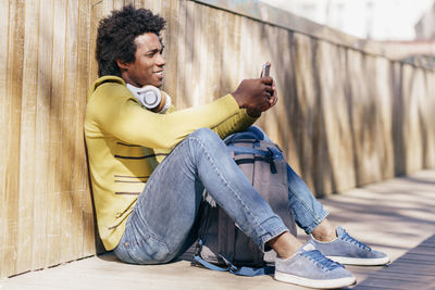 Full length of man sitting on floor while using smart phone outdoors