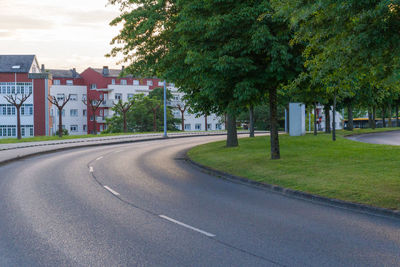 Road amidst trees and buildings against sky