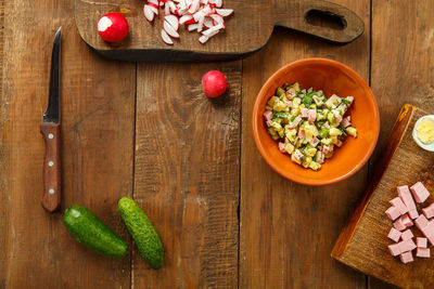 Salad in a clay plate on a table on a wooden table next to chopped vegetables and sausage 