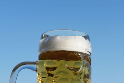 Close-up of beer glass against blue sky