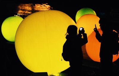 Silhouette people with balloons against sky at night