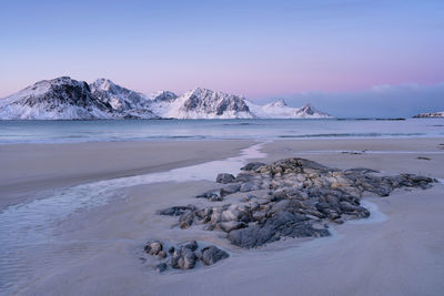 Scenic view of sea by snowcapped mountains against sky during sunset