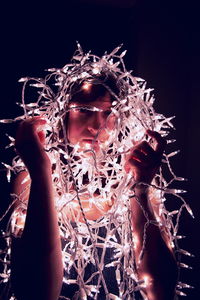 Close-up of teenage girl with illuminated string lights against black background