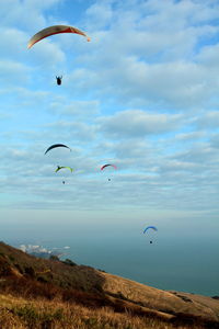 Low angle view of people paragliding over sea against sky