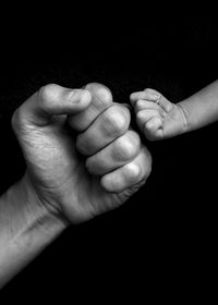 Midsection of mother and baby hand against black background