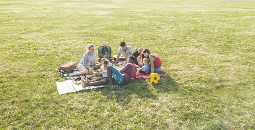 High angle view of family friends sitting on grassy field during picnic