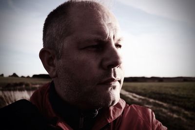 Portrait of man looking away on field against sky