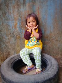 Full length of cute girl sitting on tire against wall