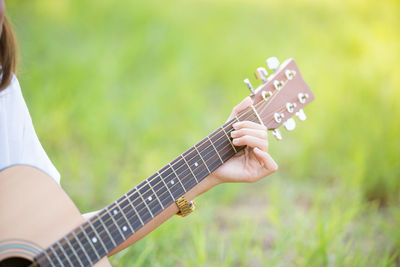 Cropped hand of woman playing guitar on field