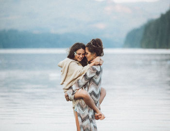 Mother holding her daughter walking i the water with mountains, and the lake 