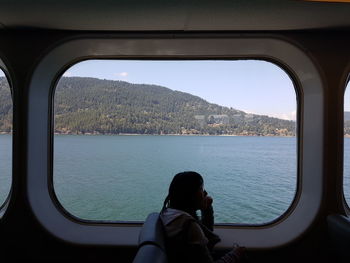 Side view of woman looking at sea through window in boat