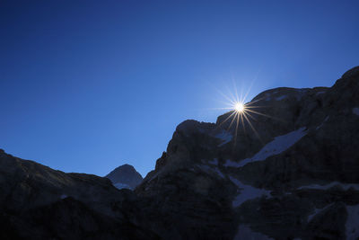 Low angle view of snowcapped mountains against clear blue sky