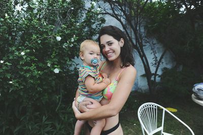 Portrait of happy mother holding baby while standing against trees