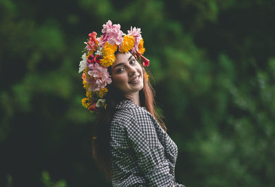 Portrait of smiling young woman wearing flowers against trees
