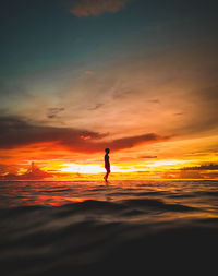 Low section of man walking on beach against sky during sunset