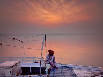 Full length of mature man sitting in boat on sea against sky during sunset