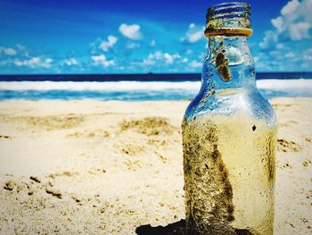 Close-up of glass bottle on sand at beach against sky