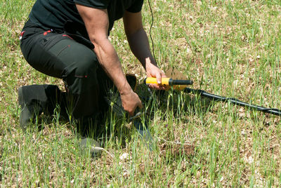 Metal detecting - low section of man in a field with metal detector, pinpointer and digger knife.