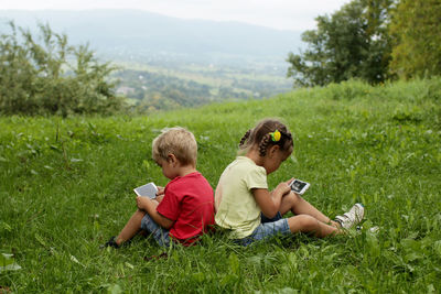 Cute little children, boy and girl, sitting back to back and sharing a photo on social media