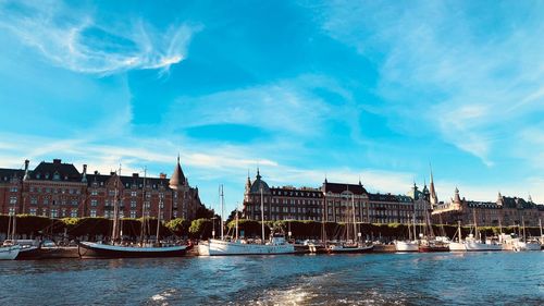 Sailboats in river by buildings against sky