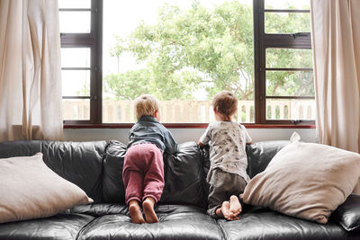 Rear view of mother and daughter sitting on bed at home