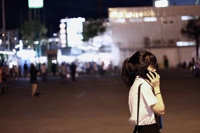 Woman in white shirt standing on street is using the phone in city at night