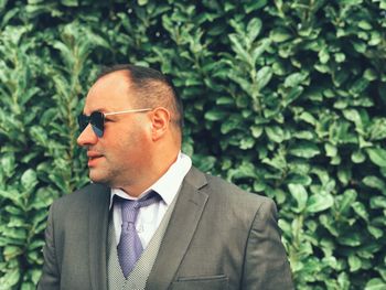 Businessman wearing sunglasses against plants