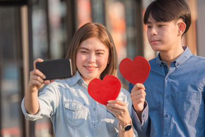 Couple doing selfie while holding heart shape outdoors