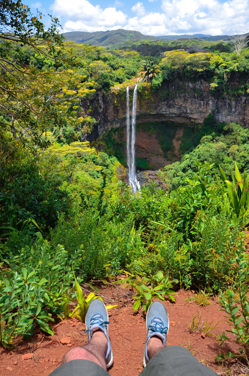 LOW SECTION OF PERSON STANDING BY WATERFALL AGAINST PLANTS