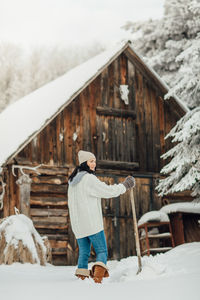 Smiling young woman standing on snow field against cottage