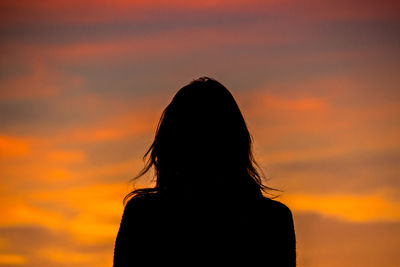 Rear view of silhouette young woman standing against orange sky during sunset