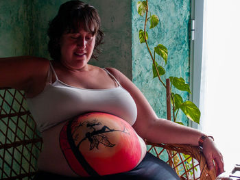 Portrait of smiling pregnant woman on seat at home