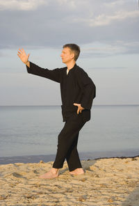 Mid adult man practicing tai chi at beach against sky